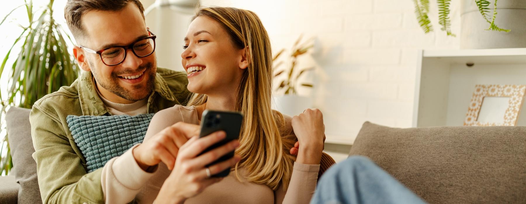 a man and a woman sitting on a couch looking at a cell phone